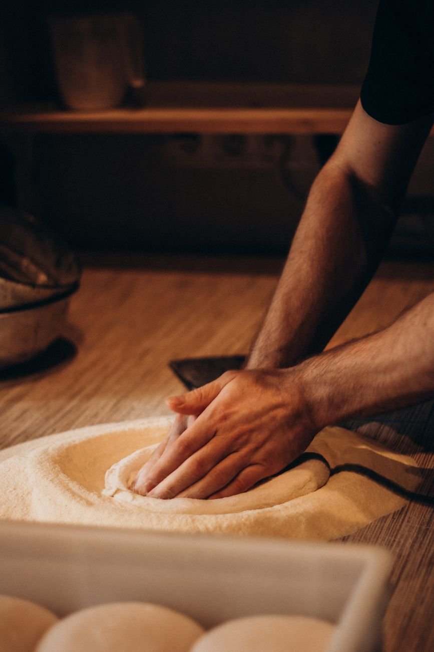 A baker's hands kneading dough in a cosy, dimly lit artisan bakery setting.